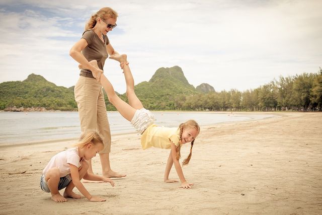 Mother playing with two young daughters on the beach while on a worldschooling travel education journey