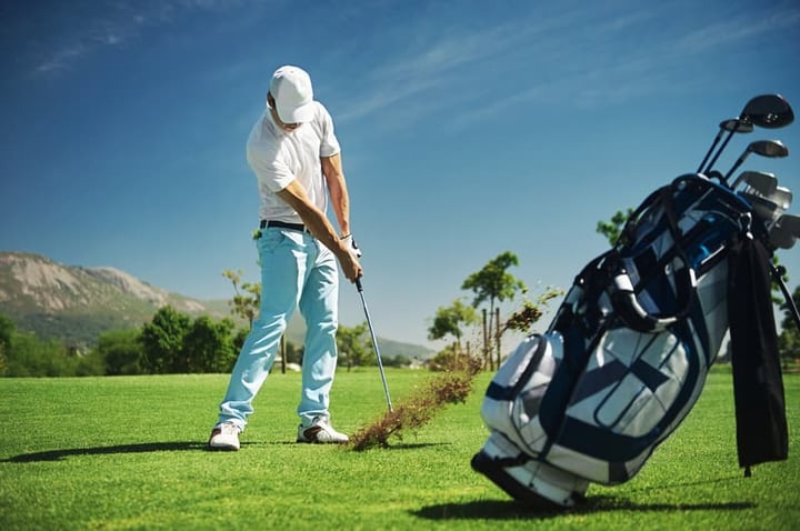 A male golfer swinging hitting a golf ball on a scenic golf course with mountain backdrop