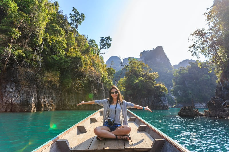 Woman smiling while traveling on a longboat in Asia with mountains in the background while on a world cruise excursion