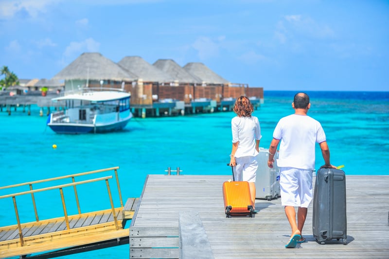 Man and woman carrying luggage on dock in the Maldives as part of their journey around the world