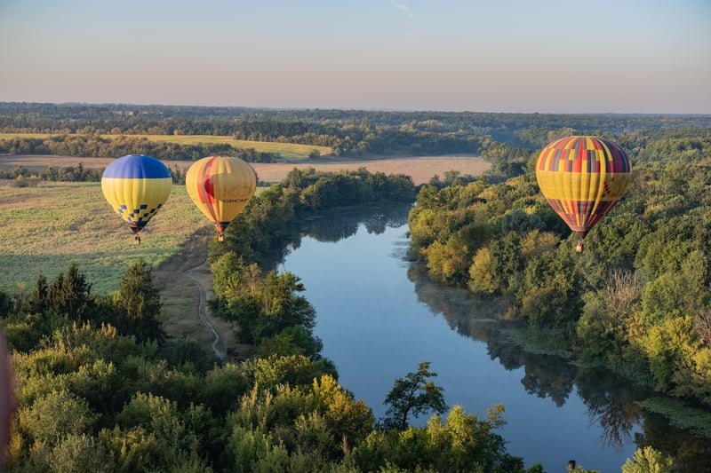 Three hot air balloons fly over wine region and river