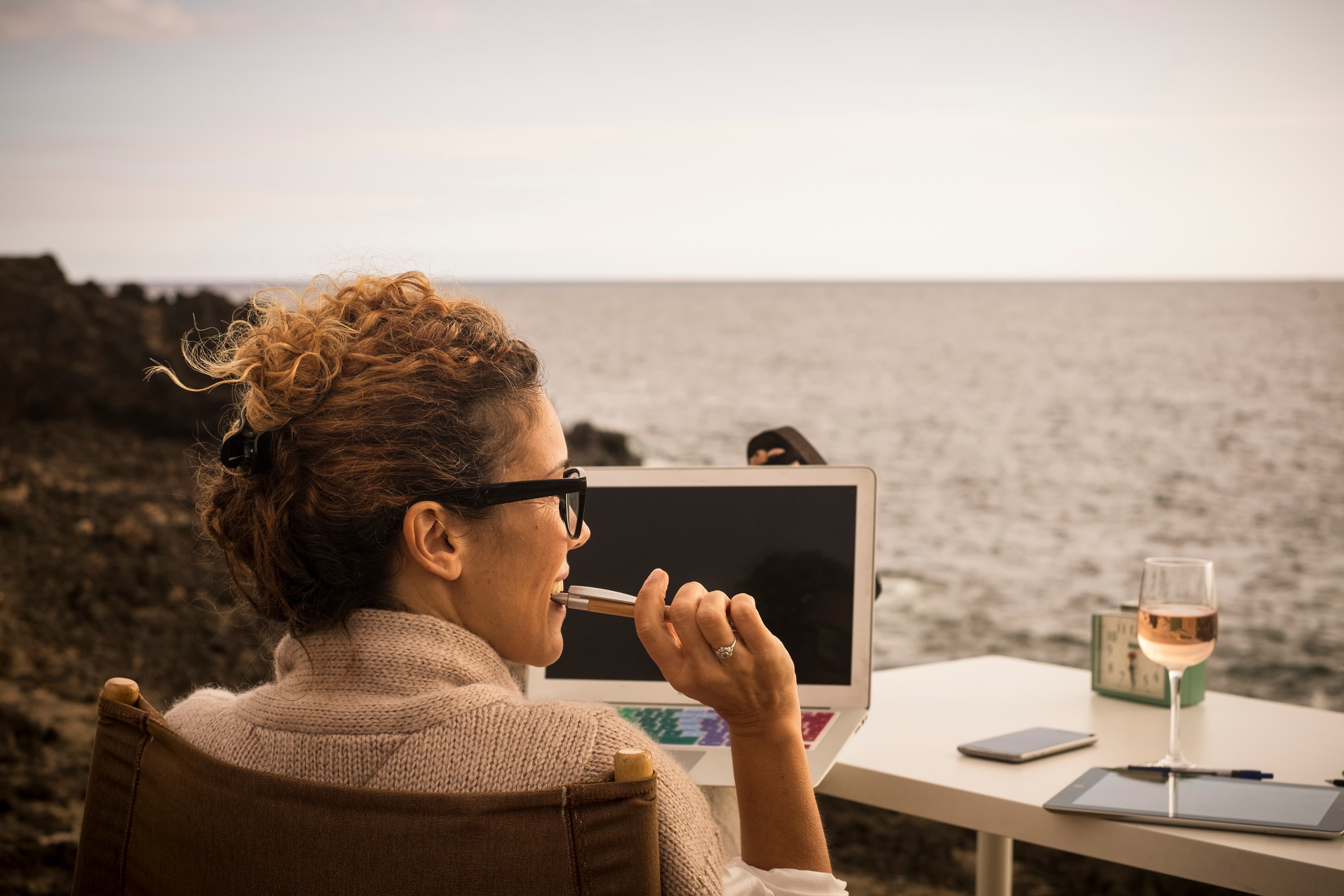 Woman working outside by the coast with a glass of wine